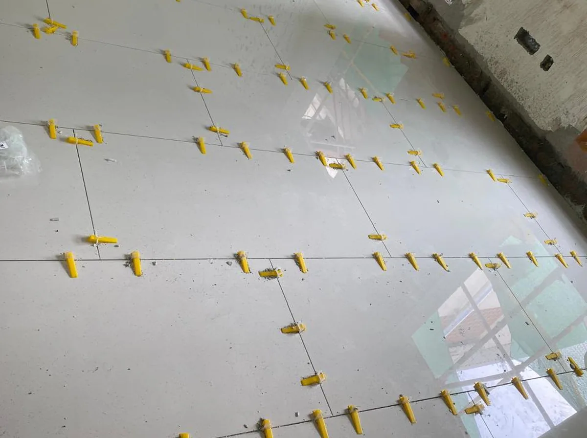 Large-format polished floor tiles being laid with yellow leveling clips on a Nexa Floors site