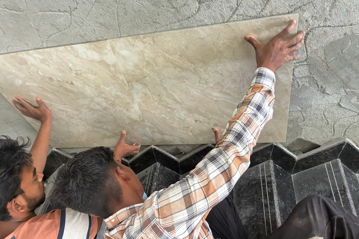 Two Nexa Floors fitters pressing a large marble-look slab into place on a wall above granite steps