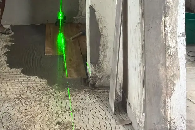 Hacked-back concrete floor being prepared, with a patch of trowelled adhesive and a green laser line marking the level