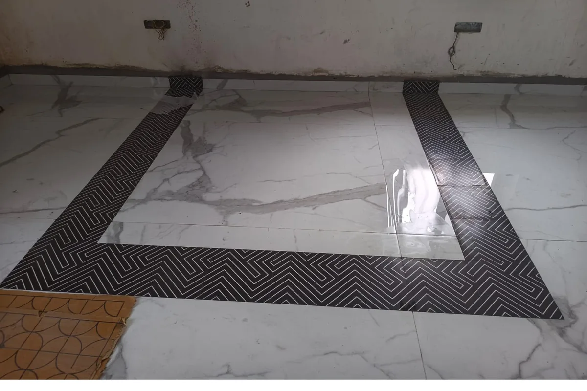 Freshly laid white marble-look floor tiles with a black-and-white geometric border, before grouting