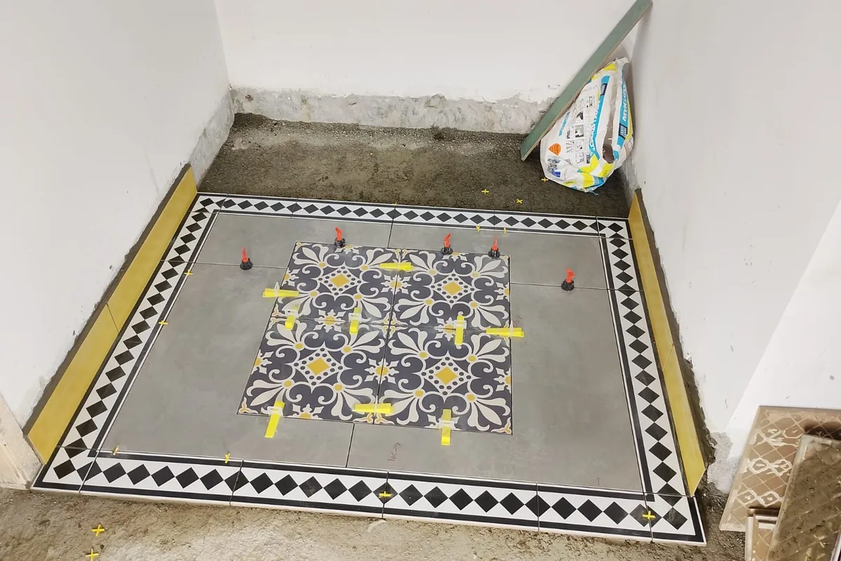 Grey floor with a central patterned tile panel and a black-and-white diamond border being set with spacers