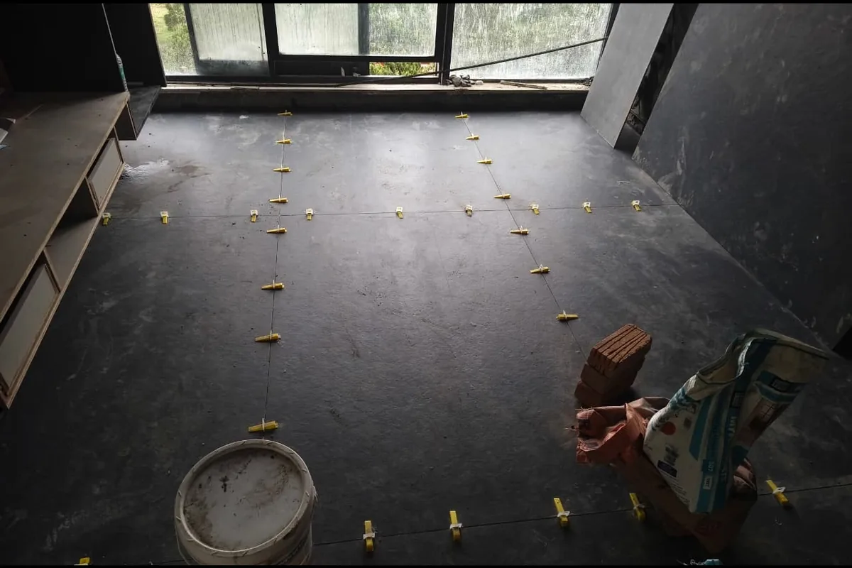 Dark grey large-format floor tiles laid with yellow leveling clips in a room under renovation