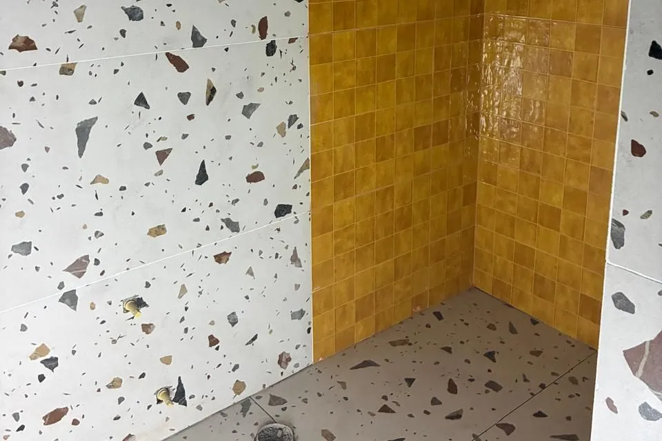Shower area with white terrazzo-look tiles on the walls and floor and a feature wall of small mustard-yellow tiles