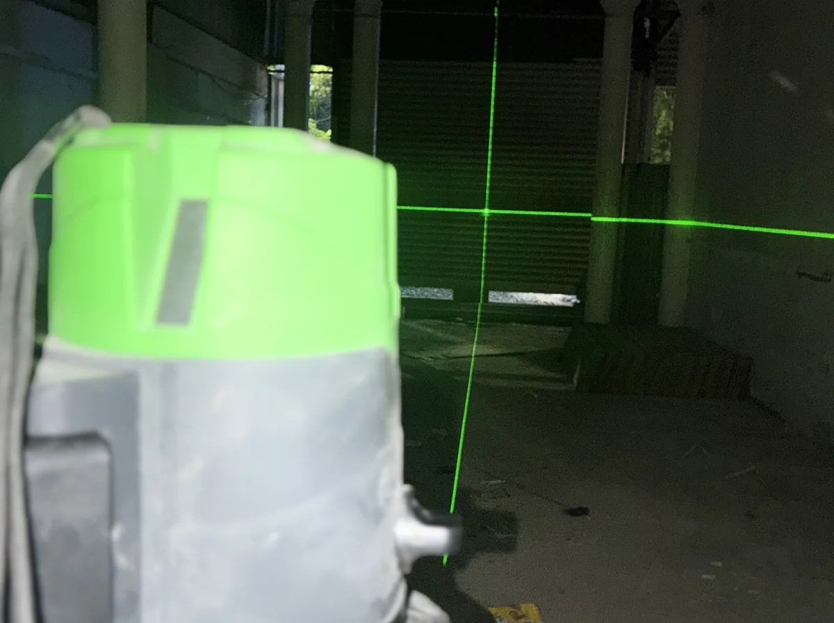 Green-beam laser levelling machine on a site floor, projecting level and plumb lines across the room